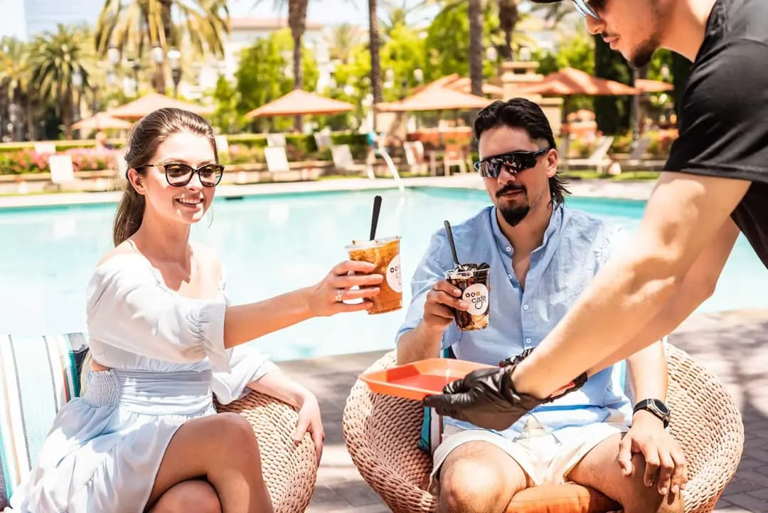 Two guests with iced drinks at an outdoor table at Le Cafe Du Parc